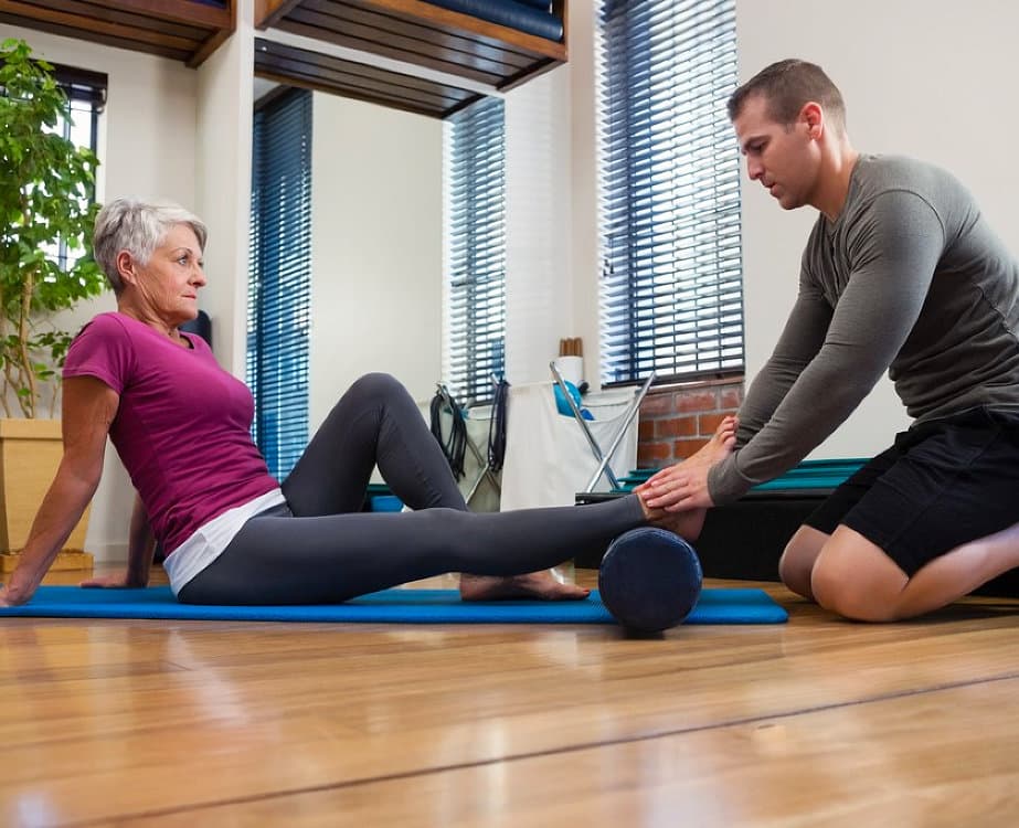adult man helping elder woman in exercing on a yoga mat